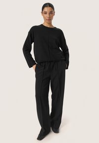 Black long-sleeve top with a round neckline, paired with loose black trousers. Both garments are made of a smooth, lightweight fabric.