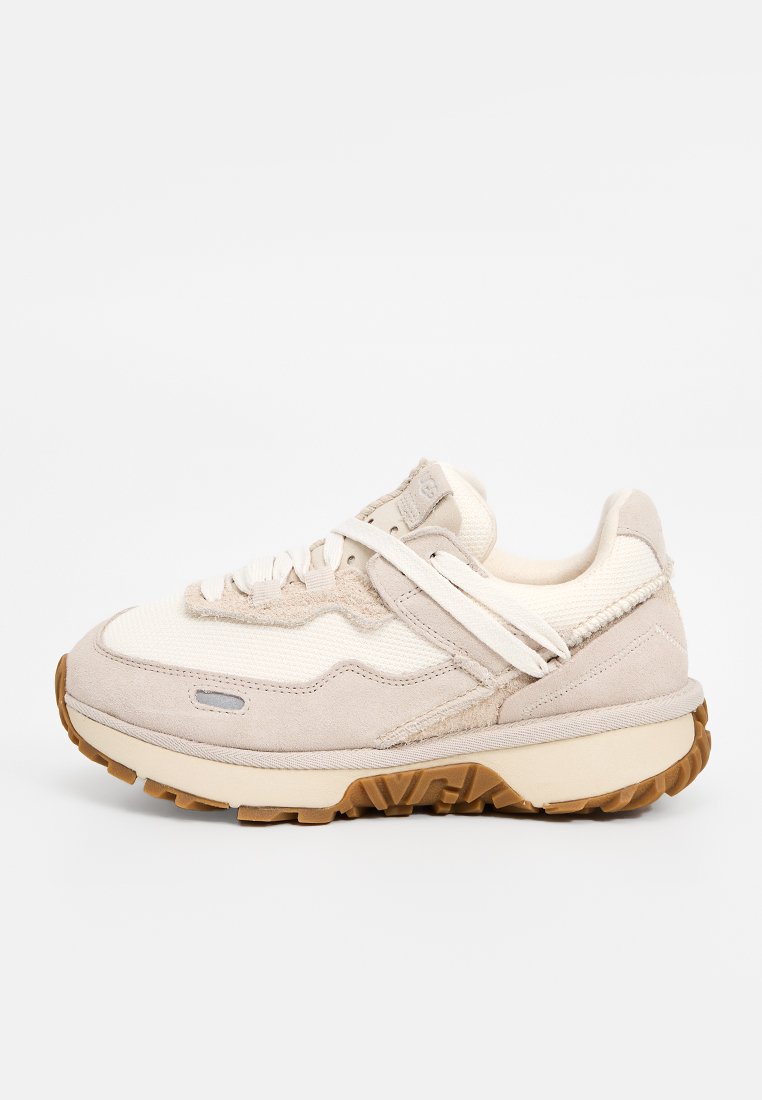 Beige sneakers met een combinatie van suede en textiel materialen, een stevige zool en een uniek ontwerp van een band over de veters.