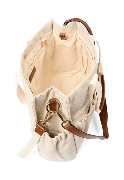 Sac fourre-tout en toile beige avec des anses en cuir marron, des ferrures dorées, un intérieur spacieux, une poche intérieure zippée et une poche latérale froncée.