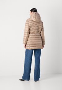 Giacca imbottita beige con cappuccio, caratterizzata da un motivo a zig zag e una vita regolabile. Abbinata a jeans blue a gamba larga.