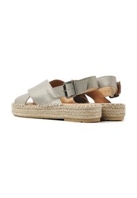 Zilverkleurige sandalen van textiel met brede kruissluitingen, verstelbare gesp en een jute-gewikkelde plateauzool. Vlak en met open achterkant.