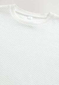 White knit pullover top with a textured pattern, featuring a rounded neckline and ribbed cuffs. Size tag displays "M."