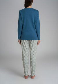 Top blu lungo con maniche, dotato di scollatura rotonda, abbinato a pantaloni da pigiama con un motivo a diamante in blu e verde.