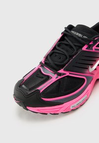 Baskets de sport noires avec des accents roses, dessus en mesh, surface texturée et design à motifs. Présente une semelle en caoutchouc noire et des lacets.