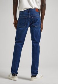 Mörkblå jeans med rak passform, tillverkade av denim, med en läderlapp på bakdelen av midjan och två bakfickor med sömnad.