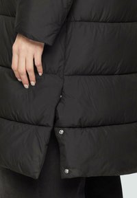Zwarte pufferjack met een gestikt patroon. Kenmerken zijn een drukknoopsluiting, een licht uitlopende zoom en een soepele, glanzende afwerking.