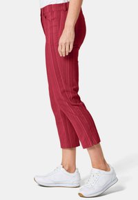 Rote Capri-Hosen mit vertikalen Streifen, ausgestattet mit einem dehnbaren Bund und frontalen Taschen, kombiniert mit weißen Sportschuhen.