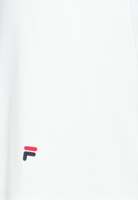 Camisa blanca de manga corta con un pequeño logo de colores rojo, azul y negro en la parte inferior izquierda. Textura de tela suave, diseño simple.