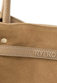 Suure plaaniga helepruun seemisnahast käekott, millel on tekstureeritud nahast ääris ja kuldse tooniga "RYŁKO" kaubamärgi kirjaga rihmal.