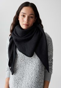 Schwarzer dreieckiger Schal mit strukturiertem Muster, um den Hals drapiert, kombiniert mit einem hellgrauen Pullover mit geschlungenem Muster.