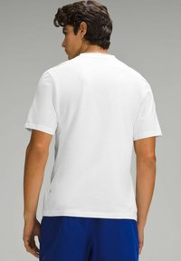 Hvid kortærmet t-shirt lavet af glat bomuld, med rund halsudskæring og et diskret logo ved kanten, parret med blå shorts.