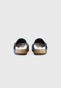 Mörkblå sandaler med korksål, mjuk vit foder och en bakre spännestrap. Slät textur med en liten klack och texturerad yttersula.