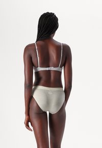 Reggiseno grigio con spalline regolabili e finitura liscia, abbinato a slip a vita alta in beige chiaro con un cinturino morbido.