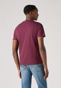 Kurzärmliges, kastanienbraunes T-Shirt aus Baumwolle. Einfaches Design mit Rundhalsausschnitt und schlichter Textur, getragen mit hellblauen Jeans.