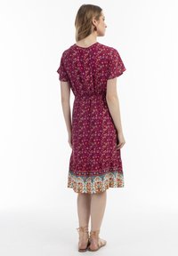 Rochie cu imprimeu floral în magenta, cu mâneci scurte tip flutter, talie elastică și tiv cu model, evidențiind accente portocalii și albastre.