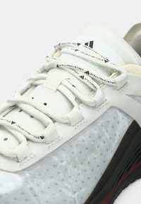 Witte sportschoen met een gestructureerd bovenwerk met een glanzende afwerking, elastische veters en branding op de tong en veterbeschermers.