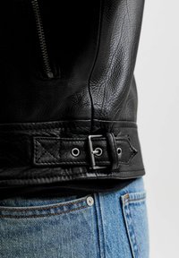 Κοντινό πλάνο στην αγκράφα και το φερμουάρ μαύρου δερμάτινου μπουφάν πάνω από τη μέση μπλε τζιν παντελονιού σε ένα άτομο.