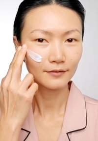 Fuktkräm som appliceras på ansiktet med ett finger. Produkten är krämig och vit. Bakgrunden är neutral och framhäver ämnet.
