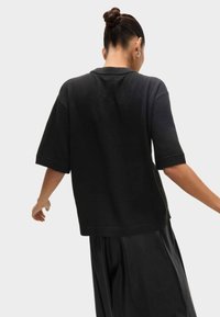 Haut en maille noir à manches courtes avec une coupe décontractée, poignets et ourlet côtelés, présentant une texture lisse et un design minimaliste.