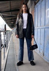 Black leather blazer, white shirt, and wide-leg blue jeans. Dark handbag with a square buckle. Black shoes. Contemporary urban setting.