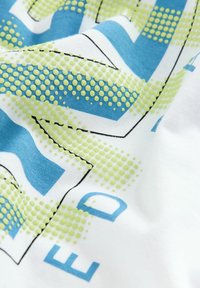 Bomuldsstof med en hvid baggrund og et blåt og grønt grafisk design, der inkluderer prikker og fede bogstaver i kontrasterende farver.