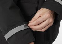 Fekete dzseki, szürke fényvisszaverő csíkkal az ujjakon. Egy kéz állítja be a dzseki ujját, kiemelve annak anyagát és szerkezetét.