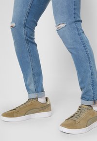 Beiga mocka sneakers med vit gummisula och snörningsdesign. Bärs med ljusblå slitna denimjeans med rivna knän.