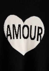 Czarny sweter z dzianiny z dużym białym sercem oraz tekstem "AMOUR" napisanym grubymi czarnymi literami, charakteryzujący się miękką fakturą.