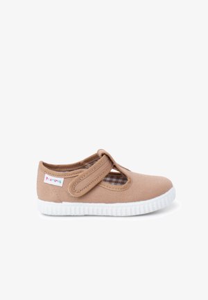 Pantof copii din pânză maro deschis cu curea velcro și talpă albă din cauciuc, având o etichetă mică cu logo pe lateral.