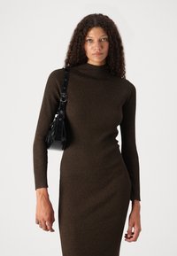 Robe marron à côtes avec un col montant et des manches longues, associée à un sac à main noir avec une courte bandoulière et une texture brillante.