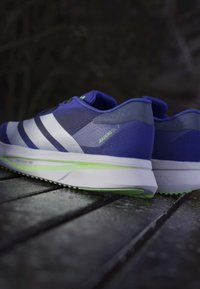 Siniset urheilukengät valkoisilla raidoilla ja vihreillä yksityiskohdilla, joissa on teksturoitu päällinen, pehmustettu varsi ja kevyt pohja.