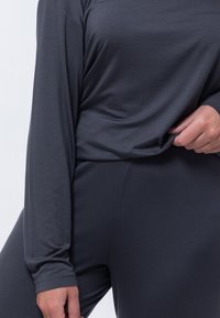 Szary, długi rękaw top wykonany z miękkiego materiału, o luźnym kroju i zwiewnym fasonie. Materiał ma subtelną teksturę i połysk.