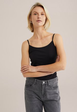 Top nero con spalline sottili, realizzato in un tessuto morbido, abbinato a jeans grigi a vita alta con chiusura a bottone e tasche laterali.