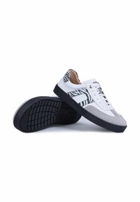 Basket basse blanche avec des accents imprimé zèbre noir, bout en daim gris et semelle noire, une chaussure reposant sur le côté de l’autre.
