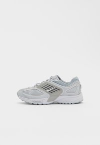 Light gray athletic shoe with mesh and synthetic material, curved design, textured accents, and white rubber sole. Side view displayed.