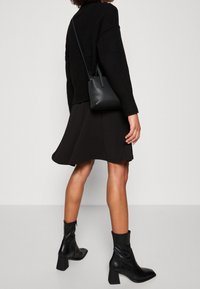Černý pletený svetr, rozšířená černá sukně, černé kožené kotníkové boty na block podpatcích a malá černá kabelka. Jednoduchý a moderní design.