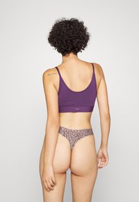 Top cropped roxo com alças finas e um fio dental bege com padrão de leopardo, apresentando um tecido suave e um design ajustado.