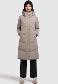 Beige padded coat with a hood and black accents, featuring a straight silhouette, large quilted sections, and side pockets. Worn with black pants.