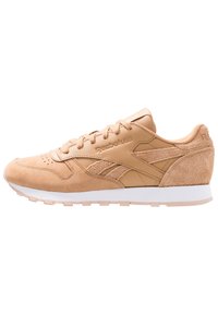 Beige Reebok-sneaker med mocka- och läderpaneler, snörning och vit sula, visad i högerprofil mot vit bakgrund.