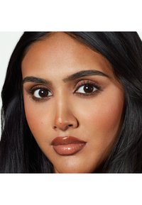 Gros plan sur un visage avec des cheveux noirs, des yeux marron et un teint lisse ; traits un maquillage doux et neutre avec des lèvres brillantes et des sourcils bien définis.
