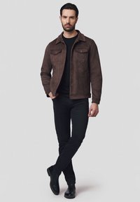 Brązowa skórzana kurtka z guzikami z przodu, dwiema kieszeniami na piersi oraz klasycznym kołnierzykiem, połączona z czarną koszulą i dopasowanymi czarnymi spodniami.