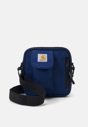 Petit sac bandoulière bleu marine avec poche avant à rabat, poche zippée, bandoulière noire réglable, et écusson logo Carhartt.