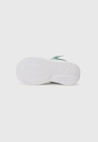 Semelle d'une chaussure de sport blanche avec un motif texturé sur la semelle, dotée d'un accent vert menthe au niveau du talon, fabriquée à partir de matériaux en caoutchouc et en mousse.