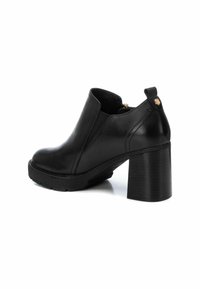 Bota de cuero negro hasta el tobillo con punta redondeada, cremallera lateral, plataforma texturizada y tacón cuadrado. Detalle de acento dorado cerca del tacón.