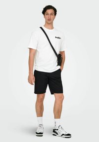 Hvid bomulds t-shirt med "Brooklyn" tryk, sorte shorts, sort crossover taske, hvide sokker og sorte og hvide sportssko.