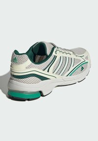 Sport shoes with a mesh upper in white and green accents, featuring a cushioned sole, laces, and a streamlined design with distinctive branding.