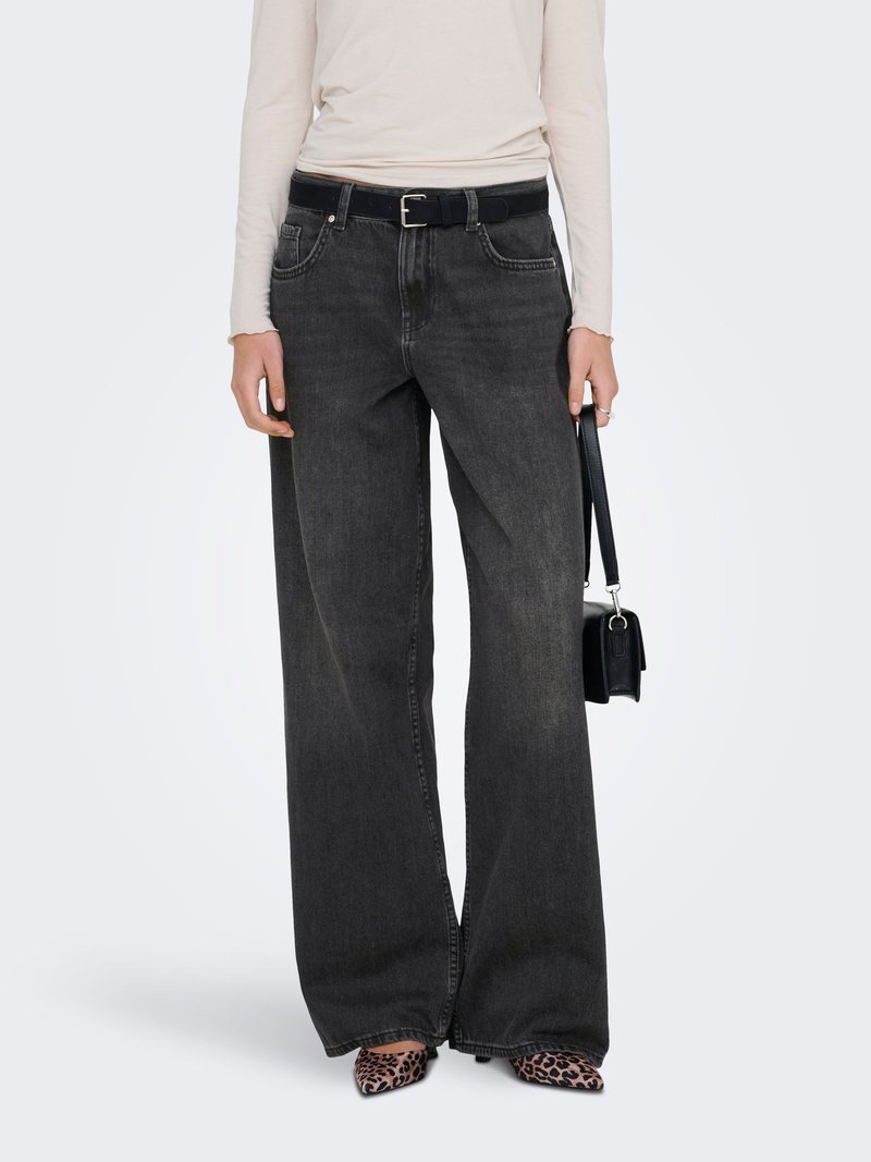 Personne portant un jean noir à jambes larges avec une ceinture noire, un haut beige à manches longues, des chaussures à motif léopard, et tenant un petit sac à main noir.