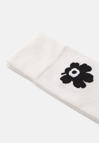 Calzini bianchi con risvolto texturizzato, caratterizzati da un grande motivo floreale nero con un cerchio bianco centrale.