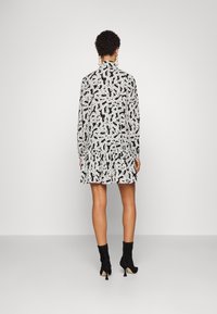 Vestido a rayas en blanco y negro con un dobladillo con volantes, mangas largas y un cuello alto, combinado con botas negras hasta los tobillos.