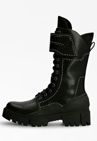 Bota de combate de cuero negro con detalles de tachuelas plateadas, cierre de cordones en la parte delantera, cuello acolchado y suela robusta. Presenta un logotipo en el lateral.